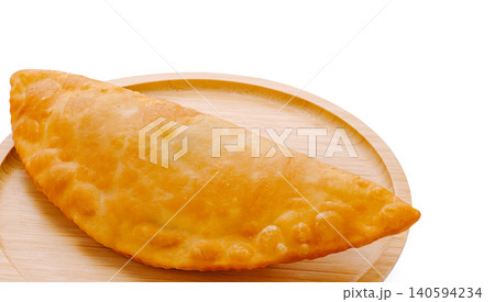 Freshly baked empanada served on a wooden plate in a kitchen setting 140594234