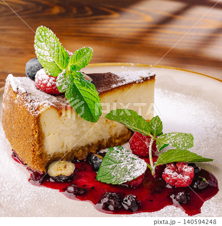Cheesecake served on a plate with berries and mint on a wooden table Cheesecake served on a plate with berries and mint on a wooden table 140594248