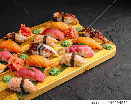 Different types of sushi served on wooden board with garnishes and sauces 140594272