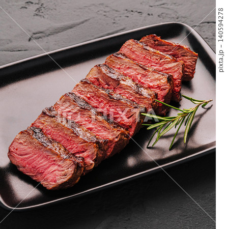 Grilled veal steak served on black plate with fresh rosemary garnish in kitchen Grilled veal steak served on black plate with fresh rosemary garnish in kitchen 140594278