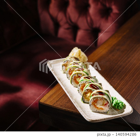 Fresh sushi rolls served on a plate beside a deep red sofa in a restaurant Fresh sushi rolls served on a plate beside a deep red sofa in a restaurant 140594286