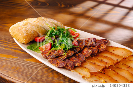 Sliced meats and bread served on a plate with greens and tomatoes Sliced meats and bread served on a plate with greens and tomatoes 140594338