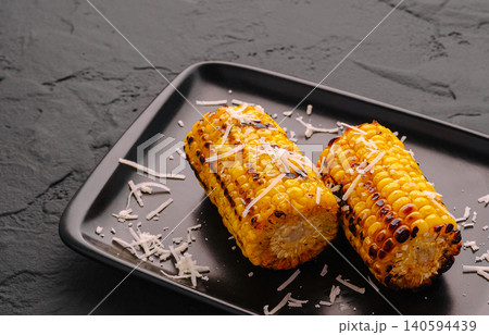 Grilled corn served on a black plate with cheese on top 140594439