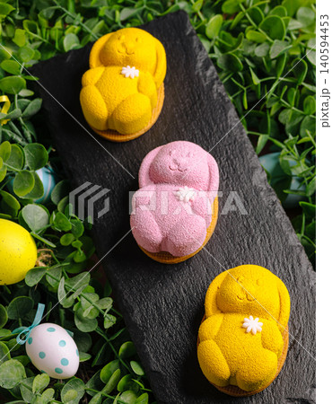 Bunny-shaped desserts on a slate board surrounded by green leaves and eggs Bunny-shaped desserts on a slate board surrounded by green leaves and eggs 140594453