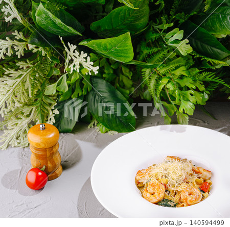 Shrimp pasta served on a white plate with greens in the background 140594499