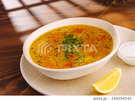 Hot soup served in a bowl with lemon and yogurt on a wooden table 140594542