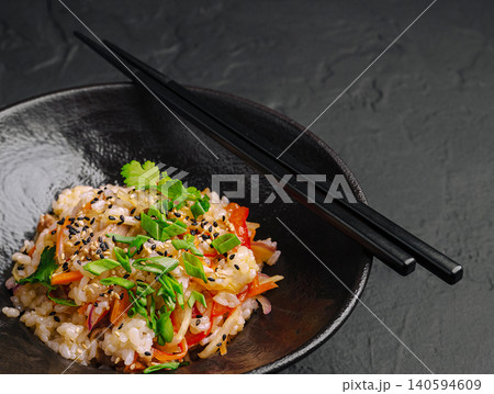 Fresh rice dish served in a black bowl with chopsticks on a dark surface 140594609