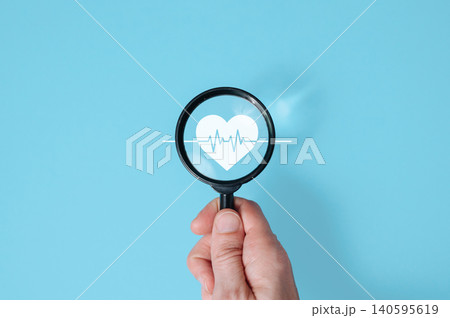 Hand holding magnifying glass over heart and cardio sign on blue background, cardiology and heart health checkup concept Hand holding magnifying glass over heart and cardio sign on blue background, cardiology and heart health checkup concept 140595619