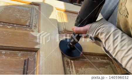 Male hands use electric polishing machine to smooth and refine wooden door surface. The rotating pad carefully treats wood, enhancing texture and finish during detailed restoration or renovation work Male hands use electric polishing machine to smooth and refine wooden door surface. The rotating pad carefully treats wood, enhancing texture and finish during detailed restoration or renovation work 140596032