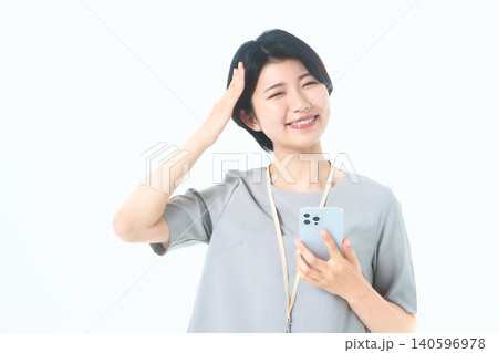 白背景でスマホを持ち頭に手を添えて笑う若い女性 白背景でスマホを持ち頭に手を添えて笑う若い女性 140596978