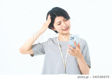 白背景でスマホを見ながら頭に手を当てる困り顔の若い女性 白背景でスマホを見ながら頭に手を当てる困り顔の若い女性 140596979