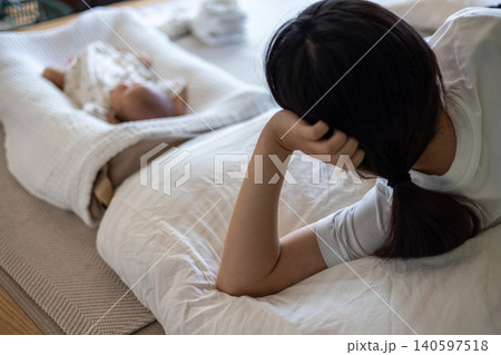 育児に疲れて新生児の側の布団に寝て肘枕している母親 140597518