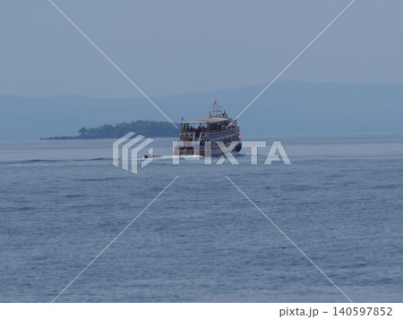 Passenger ferry boat on calm blue sea near distant island, misty horizon Passenger ferry boat on calm blue sea near distant island, misty horizon 140597852
