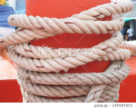 Mooring rope wrapped around red bollard at harbor dock with worn fiber texture 140597855