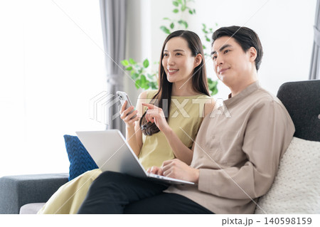 リビングでパソコンとスマホを見るミドルの夫婦 リビングでパソコンとスマホを見るミドルの夫婦 140598159