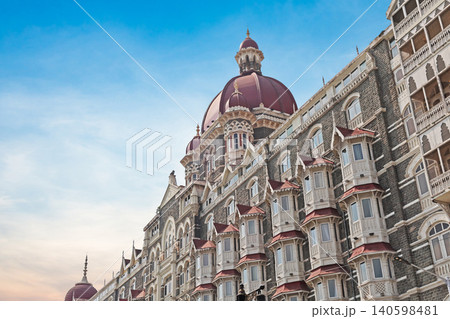 Mumbai Maharashtra India Jan 18 2026 Wide angle view of the Taj Mahal Palace Hotel facade and red domes overlooking speedboats at the harbor jetty under a bright blue sky with white clouds 140598481