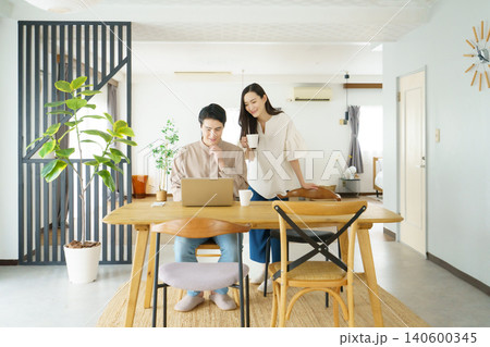自宅のテーブルでノートパソコンで作業をする男性とマグカップを持つ女性の若い日本人パワーカップル 自宅のテーブルでノートパソコンで作業をする男性とマグカップを持つ女性の若い日本人パワーカップル 140600345