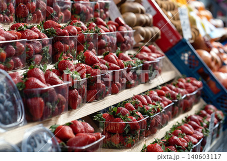 Fresh, ripe, large red strawberries with green leaves in a plastic container or box neatly displayed on a counter at a street fruit and vegetable market. Close up. Fresh, ripe, large red strawberries with green leaves in a plastic container or box neatly displayed on a counter at a street fruit and vegetable market. Close up. 140603117