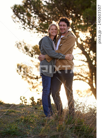 Couple, hug outdoor and portrait in park, love and support with date for bonding and time together. Sunset, nature and people in forest for fresh air, loyalty and commitment with smile for affection 140603507
