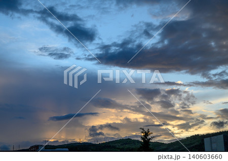 Crepuscular rays breaking through layered storm clouds at golden sunset over distant hills 140603660