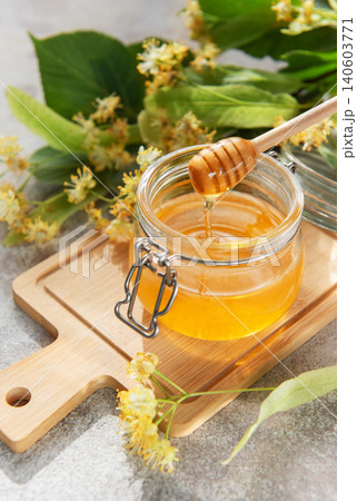 Golden linden honey jar with dipper on wooden board Golden linden honey jar with dipper on wooden board 140603771
