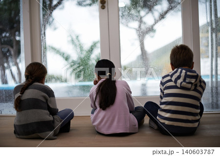 Rain, window and sad child on a floor unhappy, upset or annoyed by bad weather at home. Glass, disappointed and sibling kids in a living room frustrated by storm, cold or unexpected winter disaster 140603787