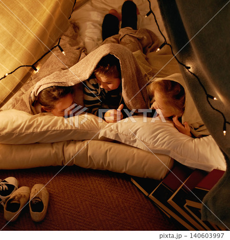 Children, happy and sleepover in tent at night with conversation, bonding and holiday adventure or vacation. Young friends or kids by fairy lights, pillows and blanket at home for fun storytelling 140603997