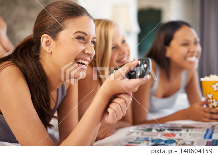 Happy friends, watching tv and eating popcorn in bedroom for streaming or bonding together at home. Television, food and group of women in bed for movie, film or laugh at funny comedy show at party 140604159