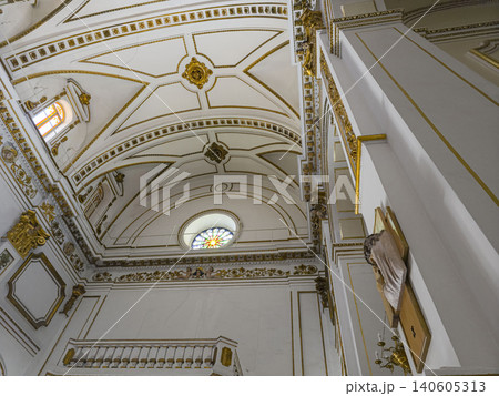 The scene shows a low angle view of a neoclassical church interior. The white vaulted ceiling features gold moldings. A colorful stained glass window adds light to the space. The scene shows a low angle view of a neoclassical church interior. The white vaulted ceiling features gold moldings. A colorful stained glass window adds light to the space. 140605313