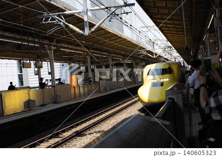 晴れた日の駅のホームに滑り込んでくる黄色い新幹線と見守る乗客たち 晴れた日の駅のホームに滑り込んでくる黄色い新幹線と見守る乗客たち 140605323