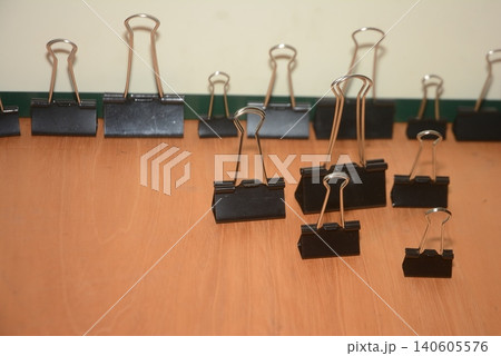 Assorted black metal binder clips arranged on a wooden desk surface Assorted black metal binder clips arranged on a wooden desk surface 140605576