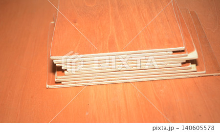 Stacked thin rectangular wooden sheets on a flat workspace surface with material 140605578