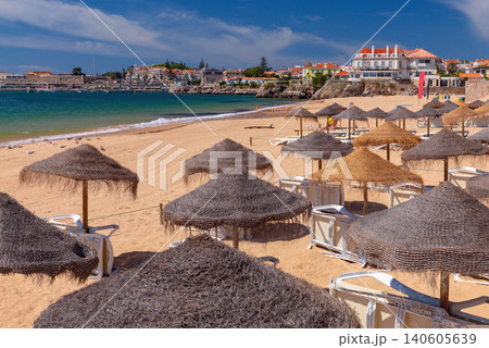 Sandy beach with traditional straw umbrellas and waterfront buildings in Cascais on the Atlantic coast of Portugal. Sandy beach with traditional straw umbrellas and waterfront buildings in Cascais on the Atlantic coast of Portugal. 140605639