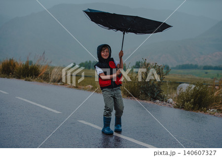 Boy standing on the road trying to hold an umbrella in rainy windy weather 140607327