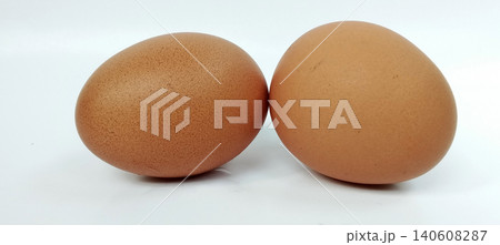 Close-up photo of two brown chicken eggs placed on a white background. 140608287