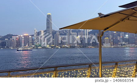 Hong Kong skyline at dusk with a ferry and illuminated waterfront promenade 140608354
