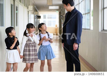 学校の廊下に並んで笑顔で立つ男性教師と女子小学生たち 140608651