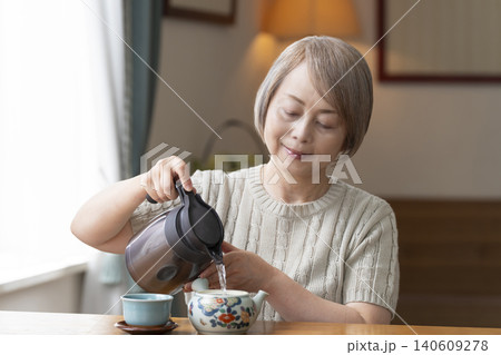 ダイニングでお茶を入れるシニア女性 140609278