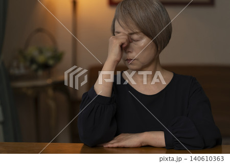 リビングで体調不良で頭をかかえるシニア女性 リビングで体調不良で頭をかかえるシニア女性 140610363