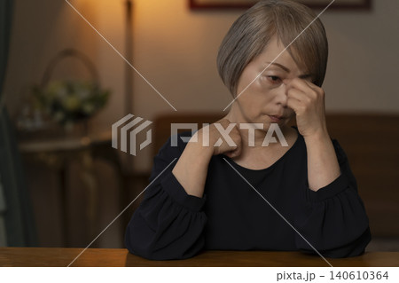 リビングで体調不良で頭をかかえるシニア女性 リビングで体調不良で頭をかかえるシニア女性 140610364