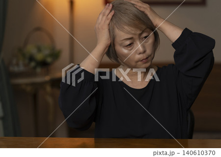 リビングで体調不良で頭をかかえるシニア女性 リビングで体調不良で頭をかかえるシニア女性 140610370