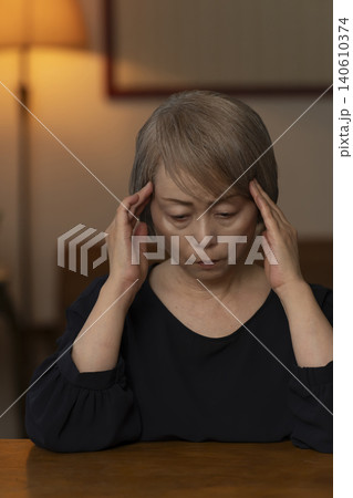 リビングで体調不良で頭をかかえるシニア女性 リビングで体調不良で頭をかかえるシニア女性 140610374