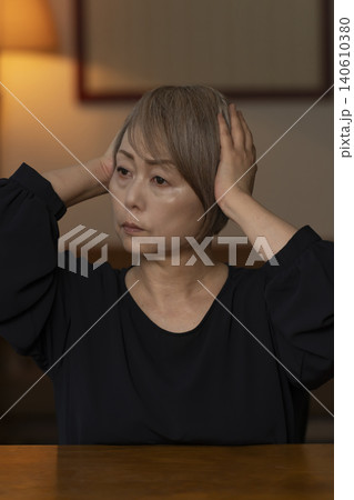 リビングで体調不良で頭をかかえるシニア女性 リビングで体調不良で頭をかかえるシニア女性 140610380
