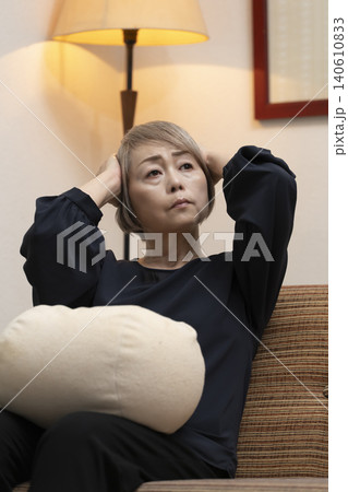 リビングのソファで体調不良で頭をかかえるシニア女性 リビングのソファで体調不良で頭をかかえるシニア女性 140610833