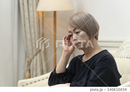 リビングのソファで体調不良で頭をかかえるシニア女性 リビングのソファで体調不良で頭をかかえるシニア女性 140610839