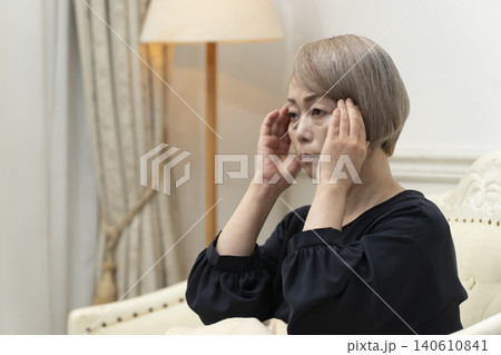 リビングのソファで体調不良で頭をかかえるシニア女性 140610841