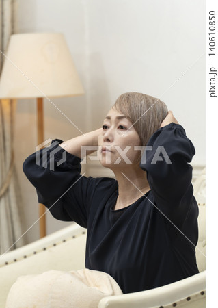 リビングのソファで体調不良で頭をかかえるシニア女性 リビングのソファで体調不良で頭をかかえるシニア女性 140610850