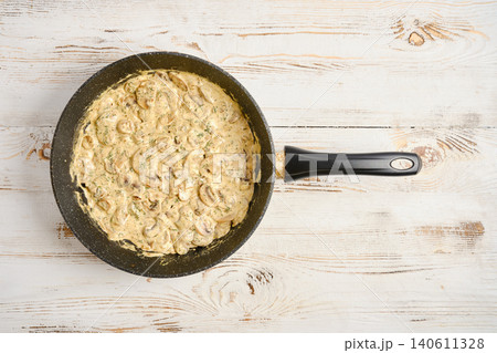 Cooking creamy mushroom dish in frying pan on light wooden table Cooking creamy mushroom dish in frying pan on light wooden table 140611328