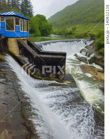 Rugged waterfall cascades over stone dam structure, vertical view Rugged waterfall cascades over stone dam structure, vertical view 140612138