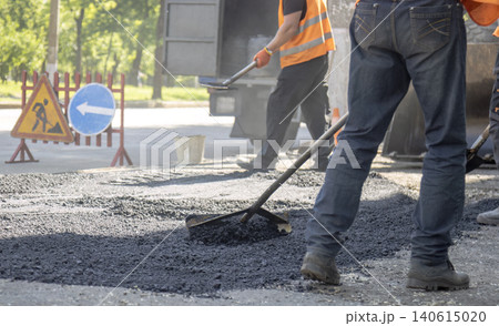 Road construction worker using a rake to level fresh asphalt with warning traffic signs in the background 140615020